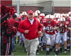 A coach leads the Cortland football team onto the field.